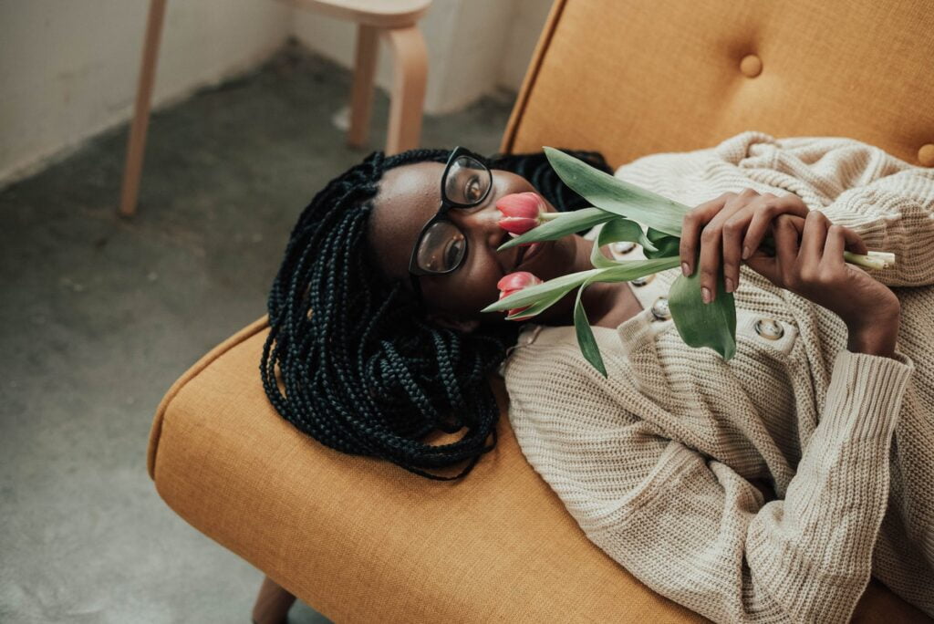 positive black lady with flowers in hands lying on sofa